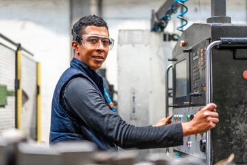 Portrait of Latin industrial worker in the metal industrial factory trade in the numerical control sector, touching the buttons on the control panel - Powered by Adobe