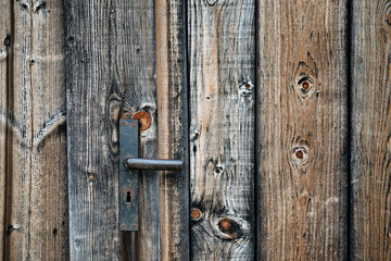Closed ancient wooden door with black metal handle and keyhole