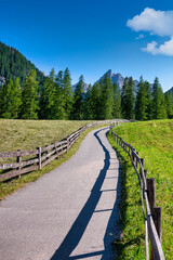 Fototapeta na wymiar Winding alpine path through green rural meadows against blue sky and dolomites mountains in Fischleintal, Trentino, South Tyrol, Italy