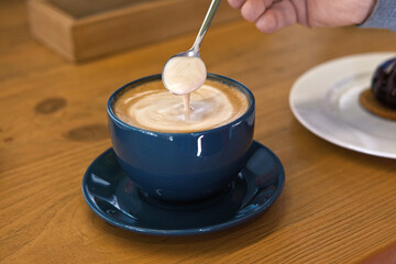 Hand is Mixing the Milk Foam of Latte. Person Stirring Cappuccino with Steel Spoon. Hot Coffee in a...
