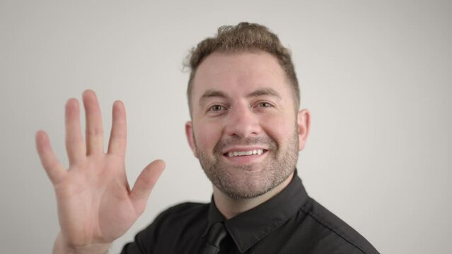 smiling man turns to camera and says hey while waving