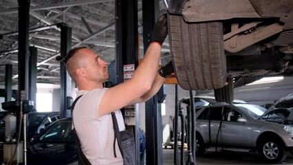 A young mechanic adjusts a tire in a repair shop in a car workshop, concentrates, lifts the tire to a raised car. 