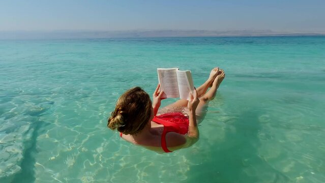 Young Woman Reads while Floating in the Dead Sea in the Jordan Rift Valley.