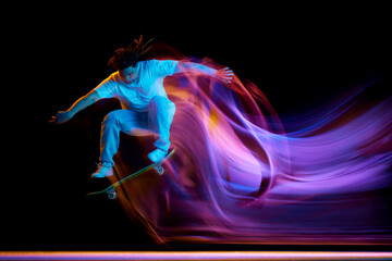 Young man, skateboarder doing jumps tricks with neon motion blur isolated black studio background....