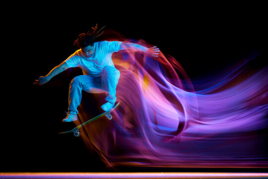 Young man, skateboarder doing jumps tricks with neon motion blur isolated black studio background. Concept of extreme kind of sport. - Powered by Adobe