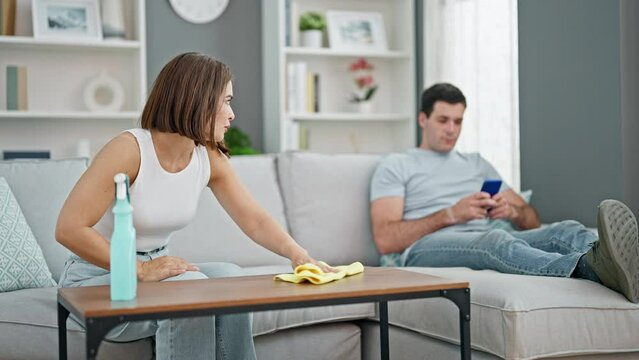 Beautiful couple cleaning while girlfriend using smartphone at home