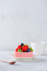 Tartlet with berries and a basket of pink chocolate in a plate with a cup of tea on a light background.
