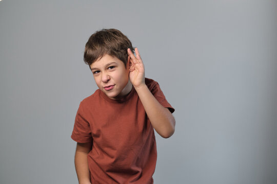 boy attentively listens, hand to ear, a gesture of focus. This image reflects the importance of listening in learning environments amid digital distractions.