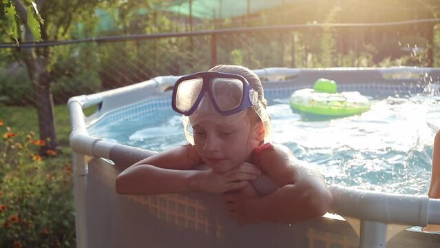 Close portrait of a young girl in a pool wearing glasses relaxing with her family in the summer at the dacha in the sunset rays. The concept of a fun summer vacation with family