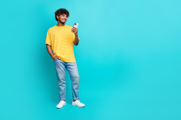 Full body photo of handsome young guy hold telephone read news dressed stylish striped yellow outfit isolated on cyan color background