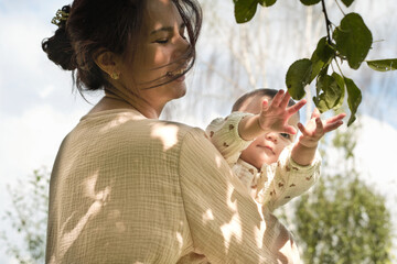 beaming young mom swings her infant gently, embracing the undeniable bond between parent and child amidst nature. Psychological Benefits of Outdoor Time for Babies