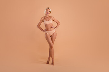 Fototapeta premium Full length photo of charming sweet senior lady dressed lingerie walking empty space isolated beige color background