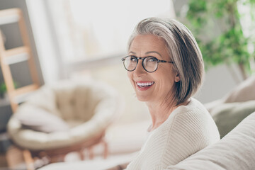 Photo of charming good mood elderly lady wear white cardigan spectacles smiling indoors apartment...