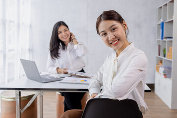 Fototapeta na wymiar Two asian confident business women point to graphs and charts to analyze market data, balance sheet, account, net profit to plan new sales strategies to increase production capacity. 