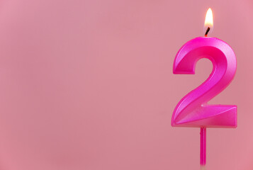 Pink birthday candle, number 2 burning on pink background. Copy space for text.