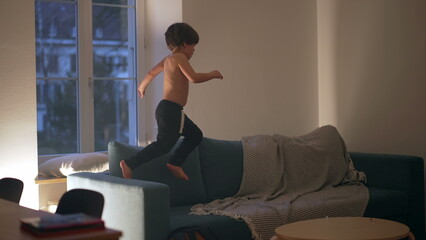 Candid child playing at night on top of sofa couch, running energetically in the evening having fun by himself in the evening