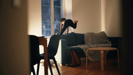 Candid small boy running and jumping on top of sofa couch at night, energetic kid having fun by...