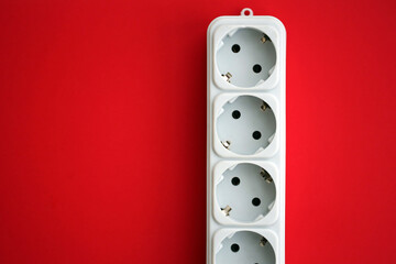 White electrical multi plug extender with european socket on bright red background close up
