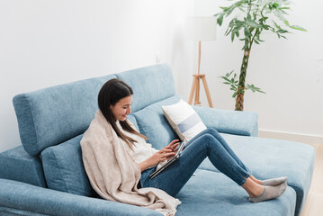 Young woman resting on sofa and using tablet in living room