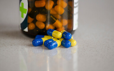 bottle with pills on marble table with blue and yellow pharmaceutical medicine capsules