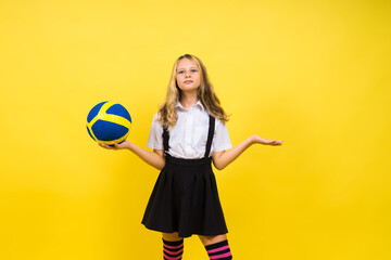 A teenager girl holds volleyball ball in hand and smiles on a red yellow background. Studio photo.