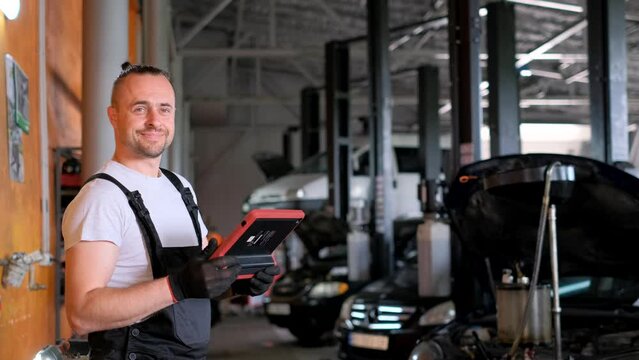 Portrait of a car mechanic with a tablet in his hands while standing in a car workshop