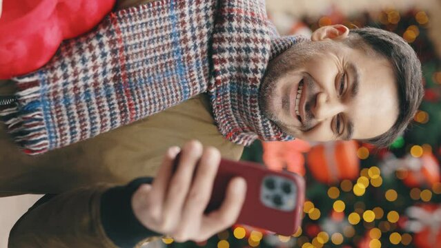 Vertical video. Handsome man walking in the street holding the valentino heart shape gift using smartphone. Smiled man outside with the red christmas present texting, scrolling.