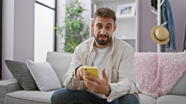 Young hispanic man using smartphone doing ok gesture at home