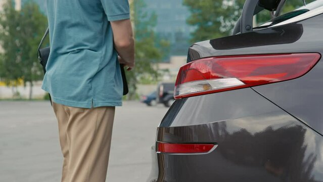 Side shot of unrecognizable driver putting baggage into car trunk space with automatic opening system