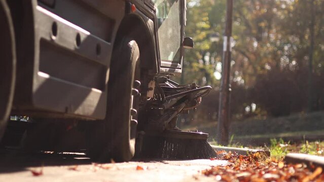 Park maintenance during autumn. Close up 4k video with an industrial vehicle with two big brushes cleaning the alleys from a park of fallen autumn leaves on the ground. selective focus.