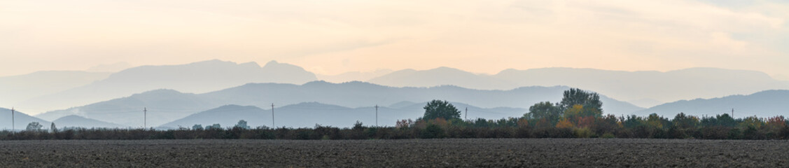 Wide panorama of mountain silhouettes and plowed farm field - obrazy, fototapety, plakaty