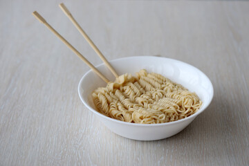 Bowl of instant cooking noodles with wooden chopsticks on white wooden table close up