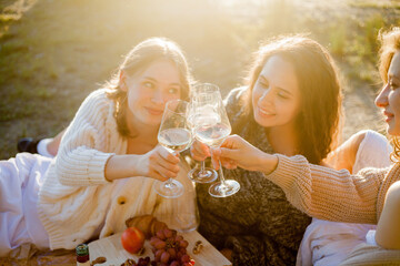Young beautiful women of 25 years old on an autumn picnic near the lake. Glass of white wine, pastries. Happy models chatting merrily. Sunset.