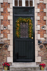 Fototapeta na wymiar Front door adorned in a Christmas atmosphere. Xmas decorations. Brick wall.