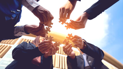 The hand of a businessman holding a paper jigsaw And solve the puzzle together. The business team assembled a jigsaw puzzle. A business group wishing to bring together the puzzle pieces - obrazy, fototapety, plakaty