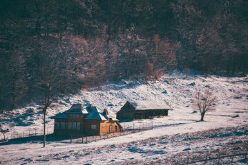 Ancient romanian houses on the frozen hills in the middle of winter. Wonderful landscape in the cold season with rustic buildings at the foot of the high mountains