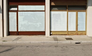 Old abandoned shop with white washed store windows at the road side. Concrete sidewalk and urban street in front. Background for copy space.