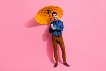 Full length photo of cheerful handsome guy using his yellow waterproof umbrella protecting against...