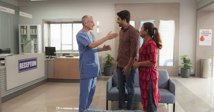 Portrait of an Indian Doctor Talking to His Patient and her Husband, Reassuring Them About Laboratory Results in a Modern Local Hospital. Medical Practitioner Sharing Good News With a Young Couple