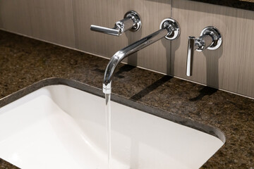 A detail of a bathroom sink with the water running with a polished chrome faucet, white sink, and a...