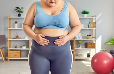 Cropped portrait of a fat overwieght woman wearing sportswear sadly looking at her big waist...