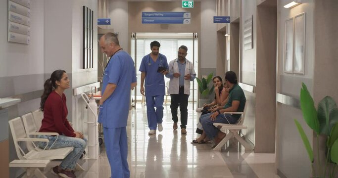 Tracking Dolly Shot of Hospital Corridor and Lobby Filled with Group of Diverse Indian Patients Waiting for their Appointments. Modern Health Clinic with Active Doctors, Nurses and Staff Working