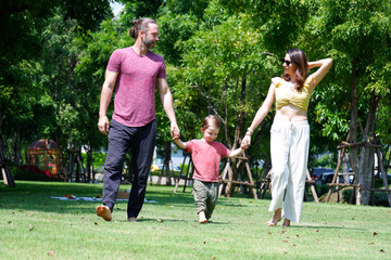 Naklejka na ściany i meble Happy father, mother and baby walking in the park.