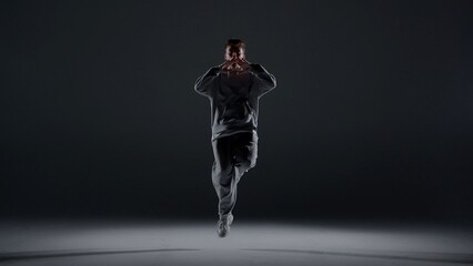 A young man stands against a dark background. He is highlighted by a white light from below....