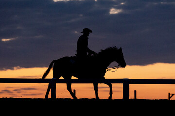 Silhouette of a western horse and rider warming up in a ring at sunrise.