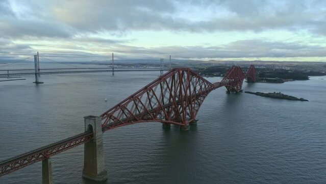 Beautiful cinematic tracking left to right high perspective aerial drone shot of Forth Rail Bridge, Scotland, Forth Road bridges in background, cars crossing bridge, clear winter day.