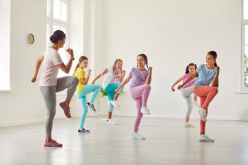 Children having a fitness workout with a trainer. Several kids doing sports exercises with a professional instructor. Group of girls in sportswear training together with a woman teacher at the gym - obrazy, fototapety, plakaty