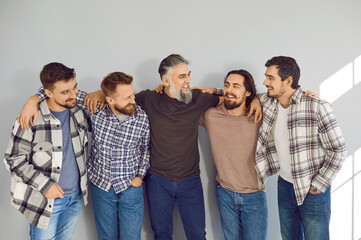 Portrait of a male mature bearded friends looking cheerful at each other and smiling on grey wall...