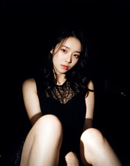 Fototapeta premium 어두운 장소의 콘트라스트가 강한 앉아있는 아시아 여성의 사진