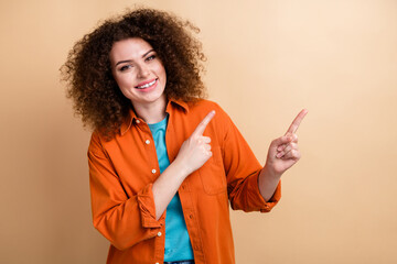 Photo portrait of lovely young lady point empty space promo dressed stylish orange garment isolated on beige color background